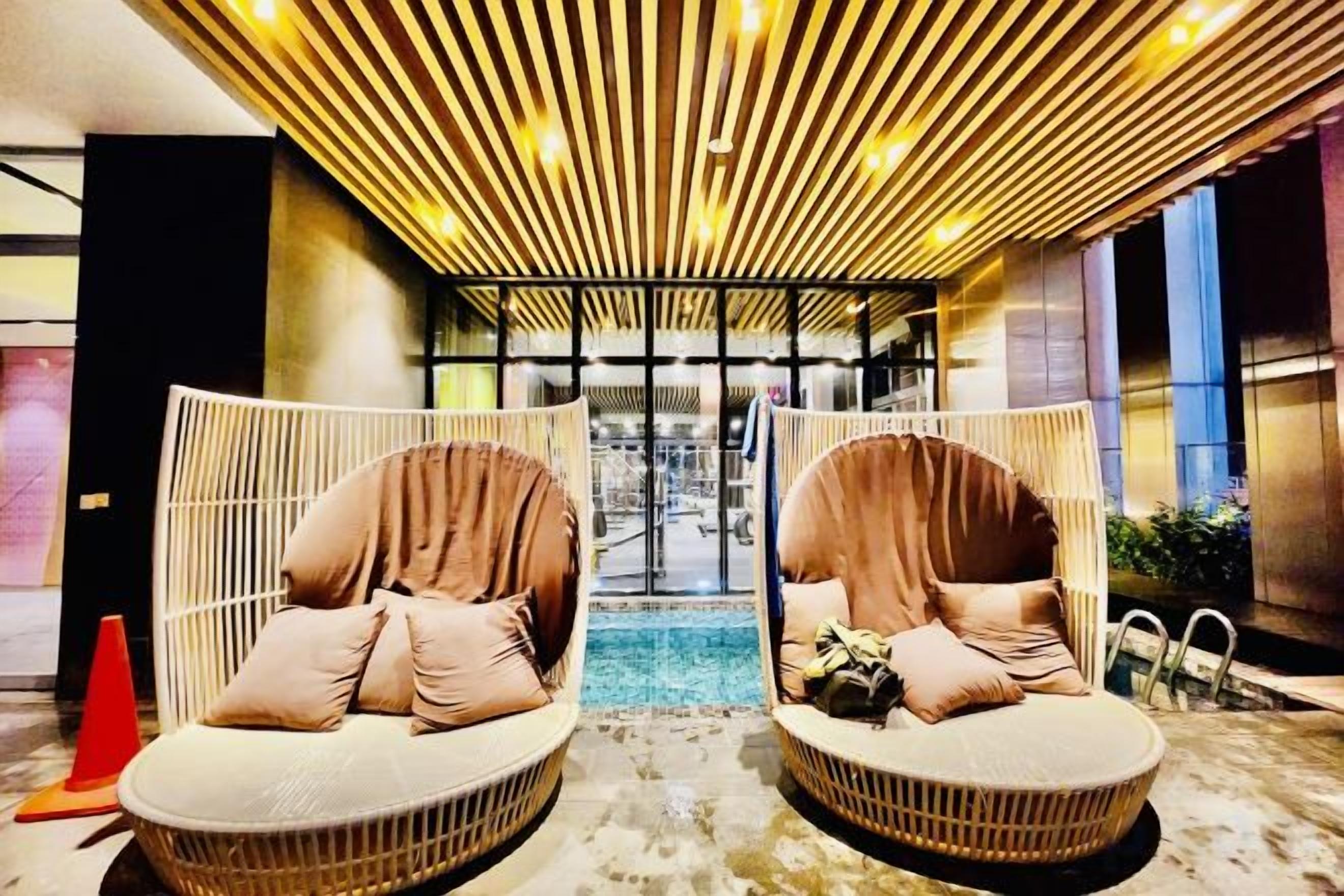 A modern interior with two wicker lounge chairs with cushions, a patterned ceiling, and a view through a glass partition.