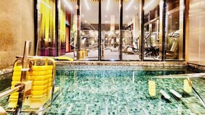 Une piscine dont le sol est carrelé, entourée de murs en verre et surmontée d’un plafond en bois.