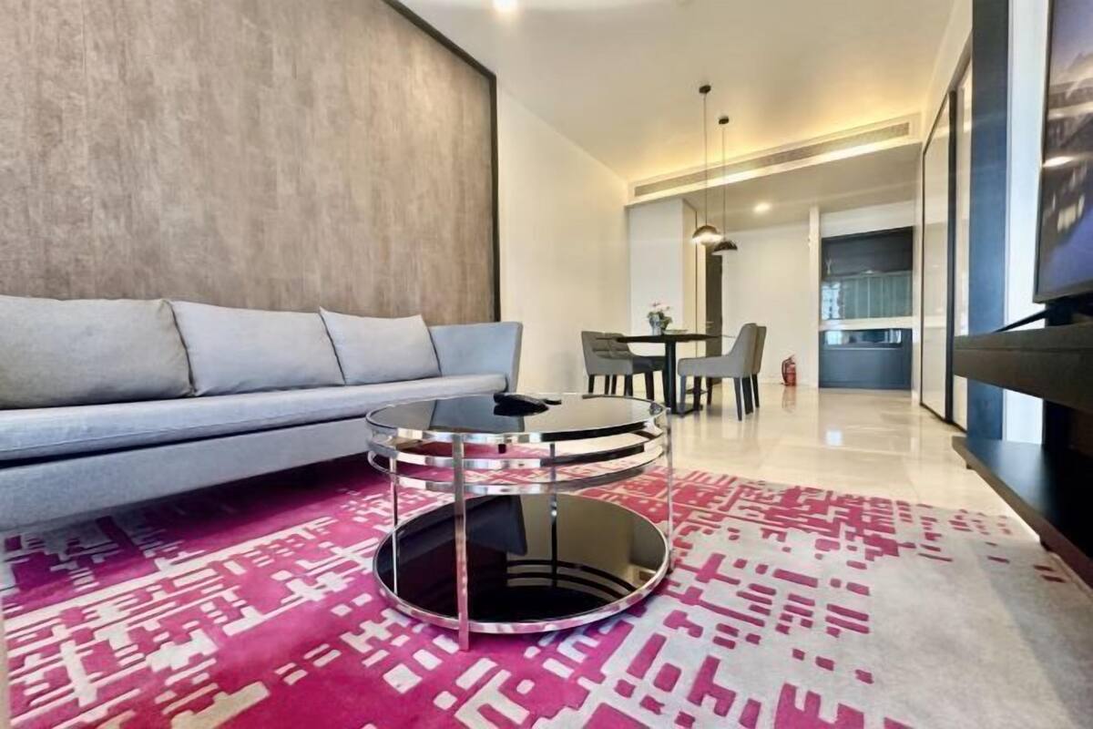 A modern living room with a grey sofa, a round glass coffee table, and a patterned rug.