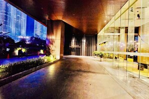 A modern building with a glass facade, a covered walkway, and a view of tall buildings in the background. - Queen Suites Tropicana The Residence by KLCC (Kuala Lumpur)