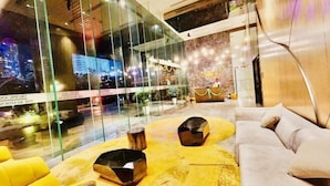 Un hall d’entrée moderne avec des murs en verre, un comptoir d’accueil et un espace détente agrémenté d’un tapis jaune et d’un canapé.