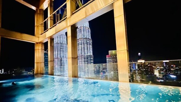 Une piscine à débordement située sur le toit, offrant une vue sur les tours Petronas la nuit.