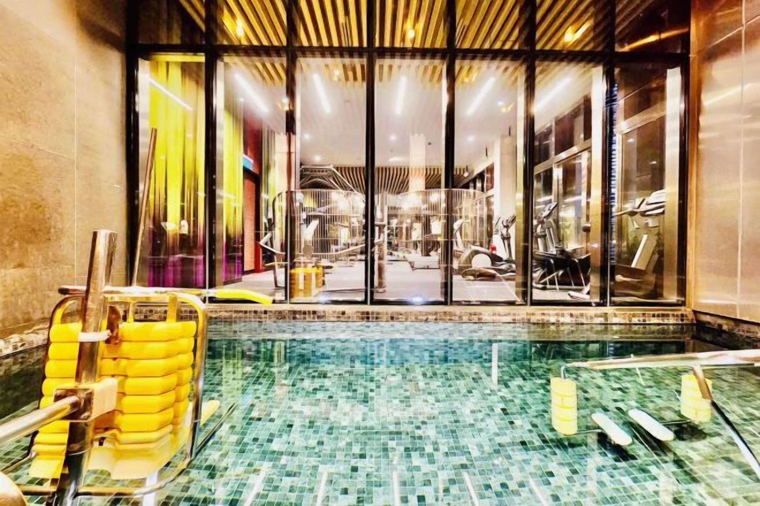 An indoor swimming pool with clear glass walls, a tiled floor, and yellow poolside chairs.