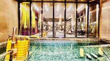 An indoor swimming pool with clear glass walls, a tiled floor, and yellow poolside chairs.