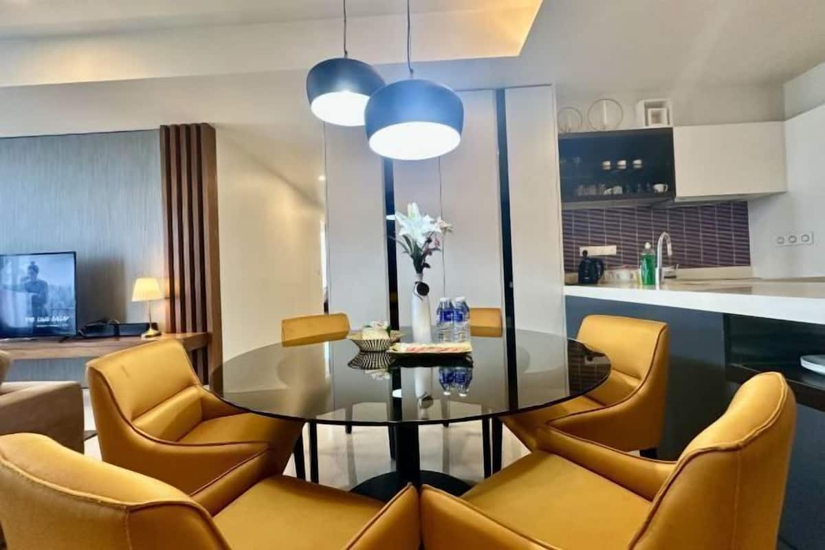 A modern dining area with a round glass table, yellow chairs, and pendant lights.