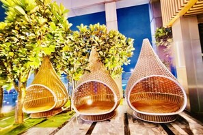 Three wicker lounge chairs with a conical design, positioned on a wooden deck with a cityscape view in the background. - Queen Suites Tropicana The Residence by KLCC (Kuala Lumpur)