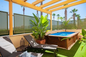 A pool area with a hot tub, lounge chairs, and tropical plants.