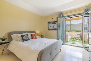 A bedroom with a bed, a nightstand, a potted plant, and a sliding glass door leading to an outdoor patio.