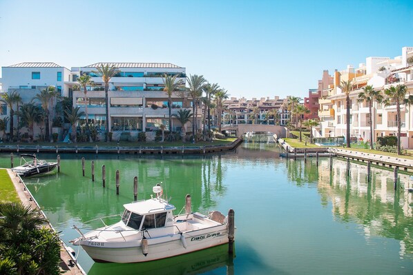 A marina with boats, a bridge, and modern buildings with balconies and palm trees.