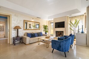 A modern living room with a sofa, blue armchairs, a coffee table, a TV, and a fireplace.