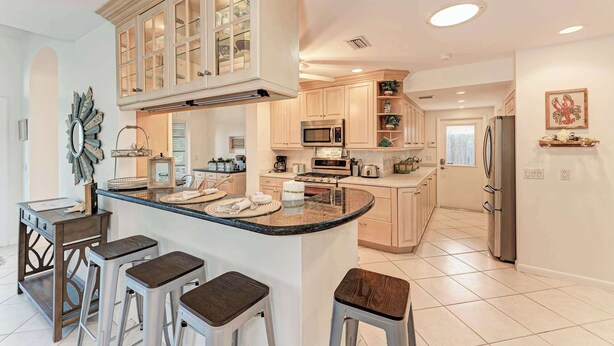 A modern kitchen with a central island, bar stools, built-in appliances, and a decorative mirror. - Cottage on Lido Key - One block to Beach, Pool (Sarasota)