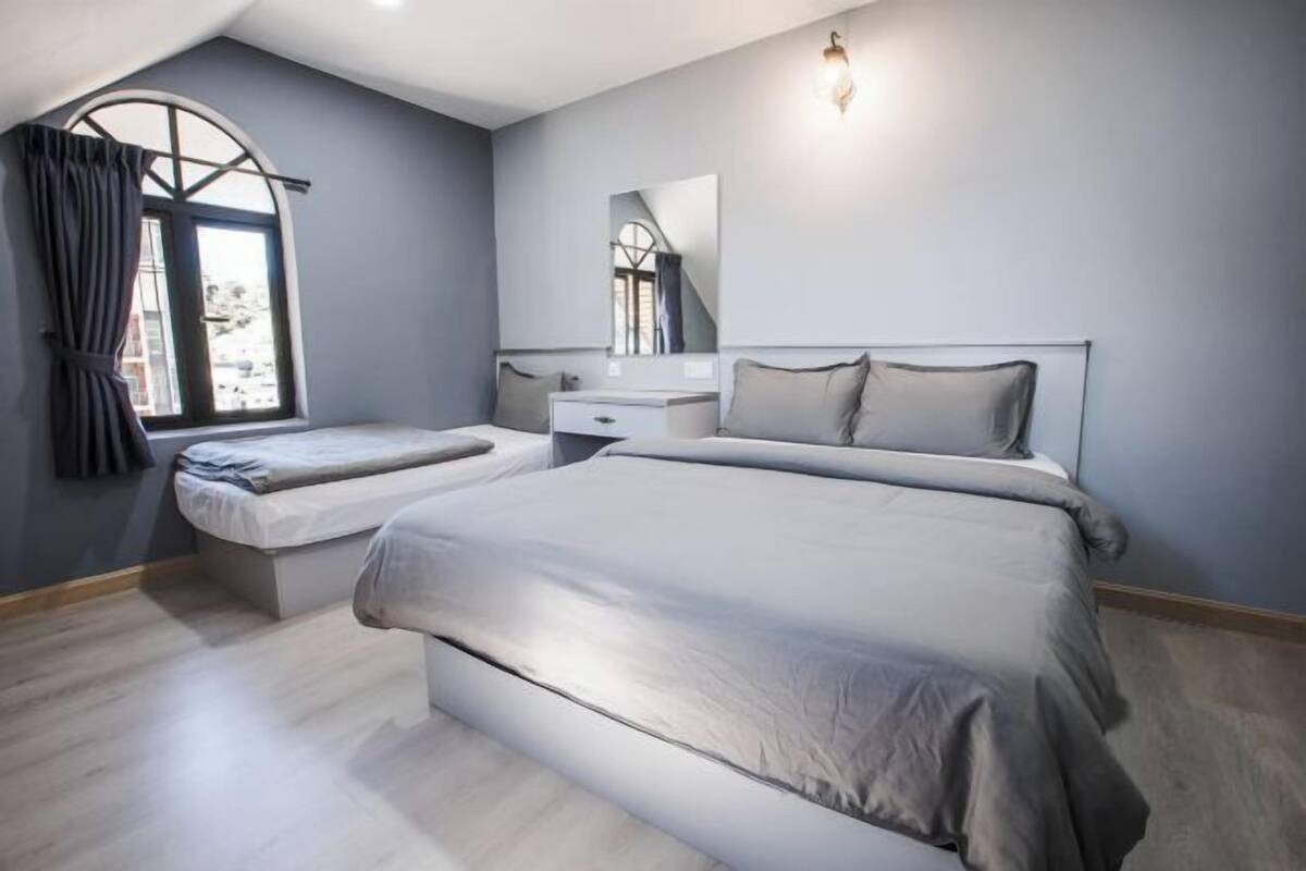 A bedroom with a large bed, a smaller bed, a vanity, and a window with curtains.