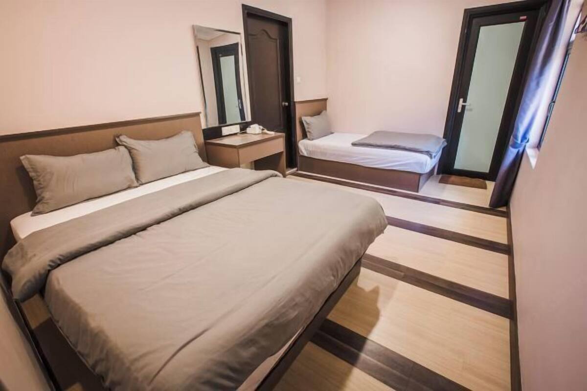 A hotel room with a large bed, a smaller bed, a bedside table with a lamp, a mirror, and a door.