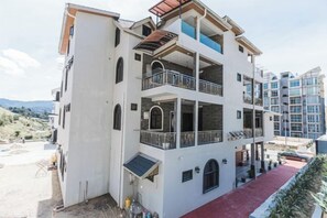 Un edificio residencial de varios pisos con balcones, un sendero rojo y montañas al fondo.