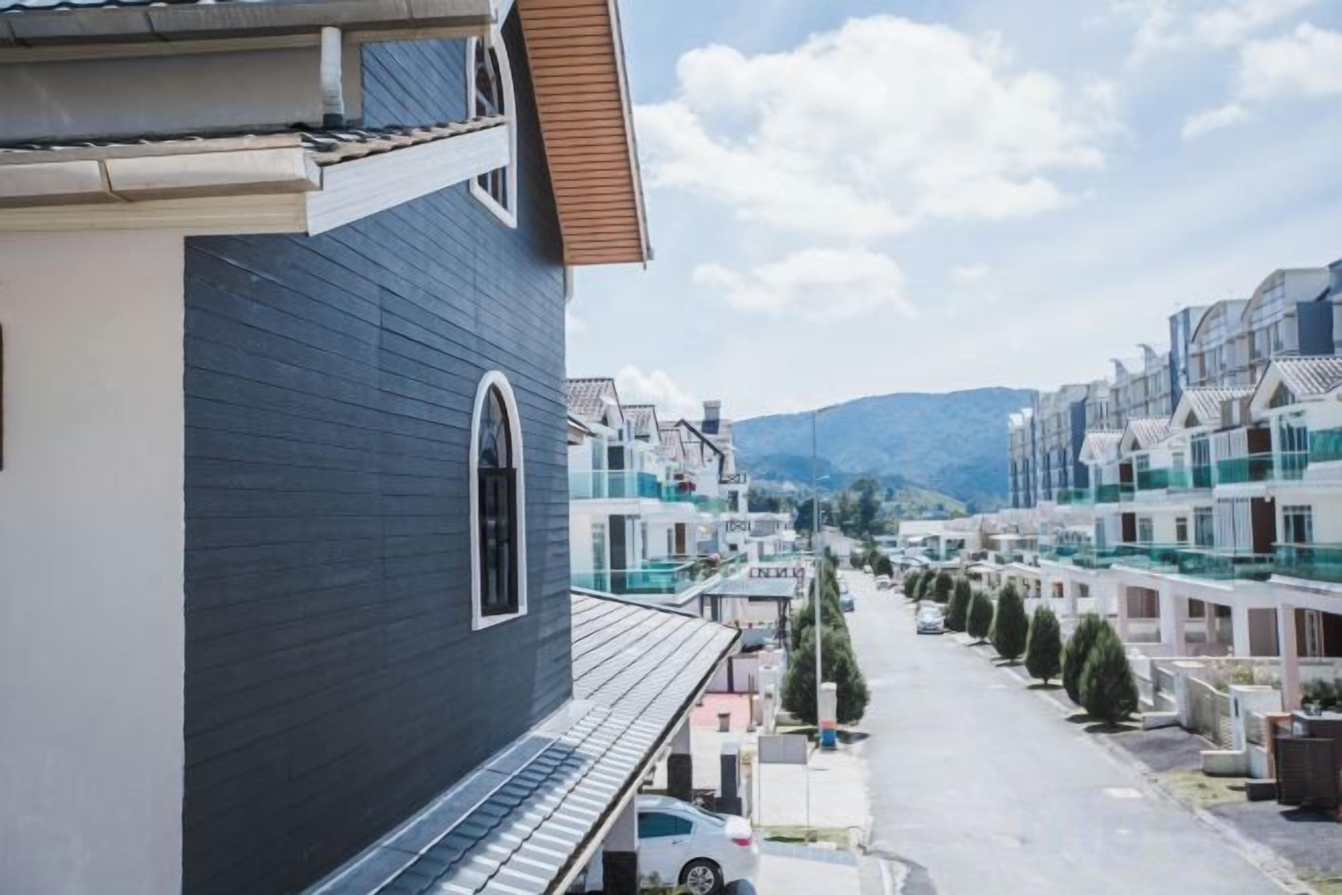 A residential street with modern houses, a clear sky, and distant mountains.