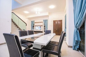 A spacious dining area with a long table and modern chairs, a staircase, and a view of the living area.