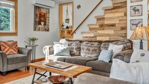 A cozy living room with a wooden staircase, a grey sofa, a wooden coffee table, and a wall with animal-themed artwork. - Pine Lantern Retreat (South Lake Tahoe)