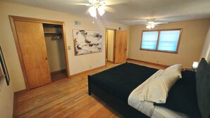 Een slaapkamer met een groot bed, een plafondventilator, een raam met zonwering en een deur naar een inloopkast.