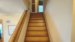 Een houten trap met een leuning, die leidt naar een deur met een 'WELCOME HOME' bord.