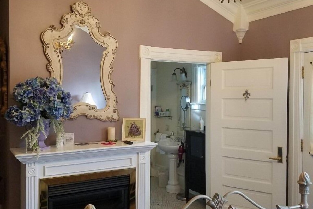 A room with a fireplace, a mirror, and a door leading to a bathroom.