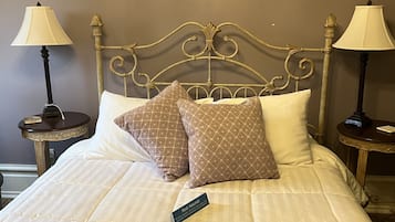 Un lit bien fait, avec une pancarte indiquant qu’il est prêt pour les invités, deux tables de chevet avec des lampes et un tableau accroché au mur.