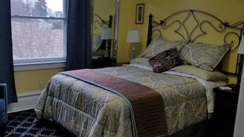 A bedroom with a bed, a nightstand, a lamp, a window with curtains, and a mirror.