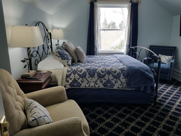 Une chambre à coucher avec un lit, une chaise, une table de chevet, une lampe et une fenêtre.