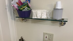 Une salle de bain avec une étagère en verre où sont rangés les articles de toilette, un porte-serviettes avec une serviette, et un interrupteur fixé au mur.