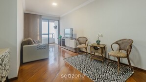 Ein modernes Wohnzimmer mit einer Couch, zwei Korbstühlen, einem gemusterten Teppich und einem kleinen Tisch mit einer Pflanze.