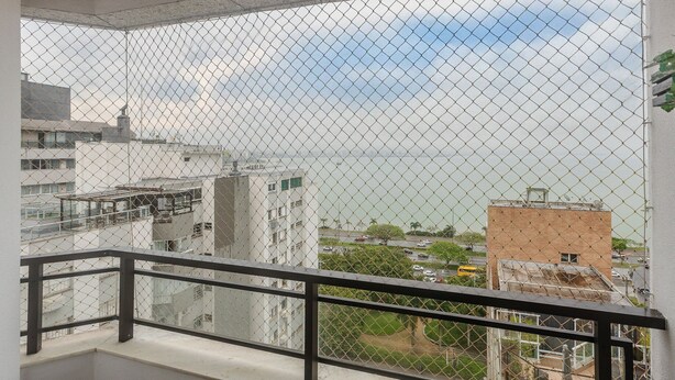 Ein Balkon mit einem Maschendrahtzaun, der auf einen Stadtblick mit Gebäuden und einem Gewässer blickt.