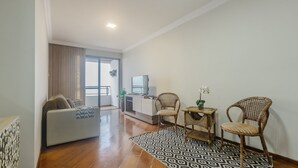 Ein modernes Wohnzimmer mit einer Couch, zwei Korbstühlen, einem gemusterten Teppich und einem kleinen Tisch mit einer Pflanze.