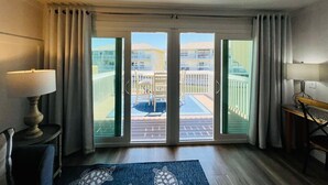 A hotel room with a large sliding glass door leading to a balcony with a pool and a view of a building with balconies. - Sandpiper Cove Unit 1047 1 Bedroom With Bonus Bunkroom FREE Beach Service (Destin)