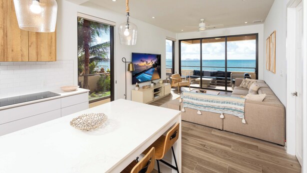 A modern kitchen with a large island, a dining area with a view of the ocean, and a living room with a sofa and a TV. - SeaDreams 1: Ocean Condos w/Pool. Jacuzzi & Rooftop Patio; Stay a Week, Save 20% (West Bay)