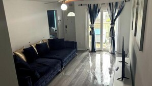 Un salon avec un canapé bleu foncé, un ventilateur de plafond et une porte-fenêtre coulissante donnant sur un espace extérieur.