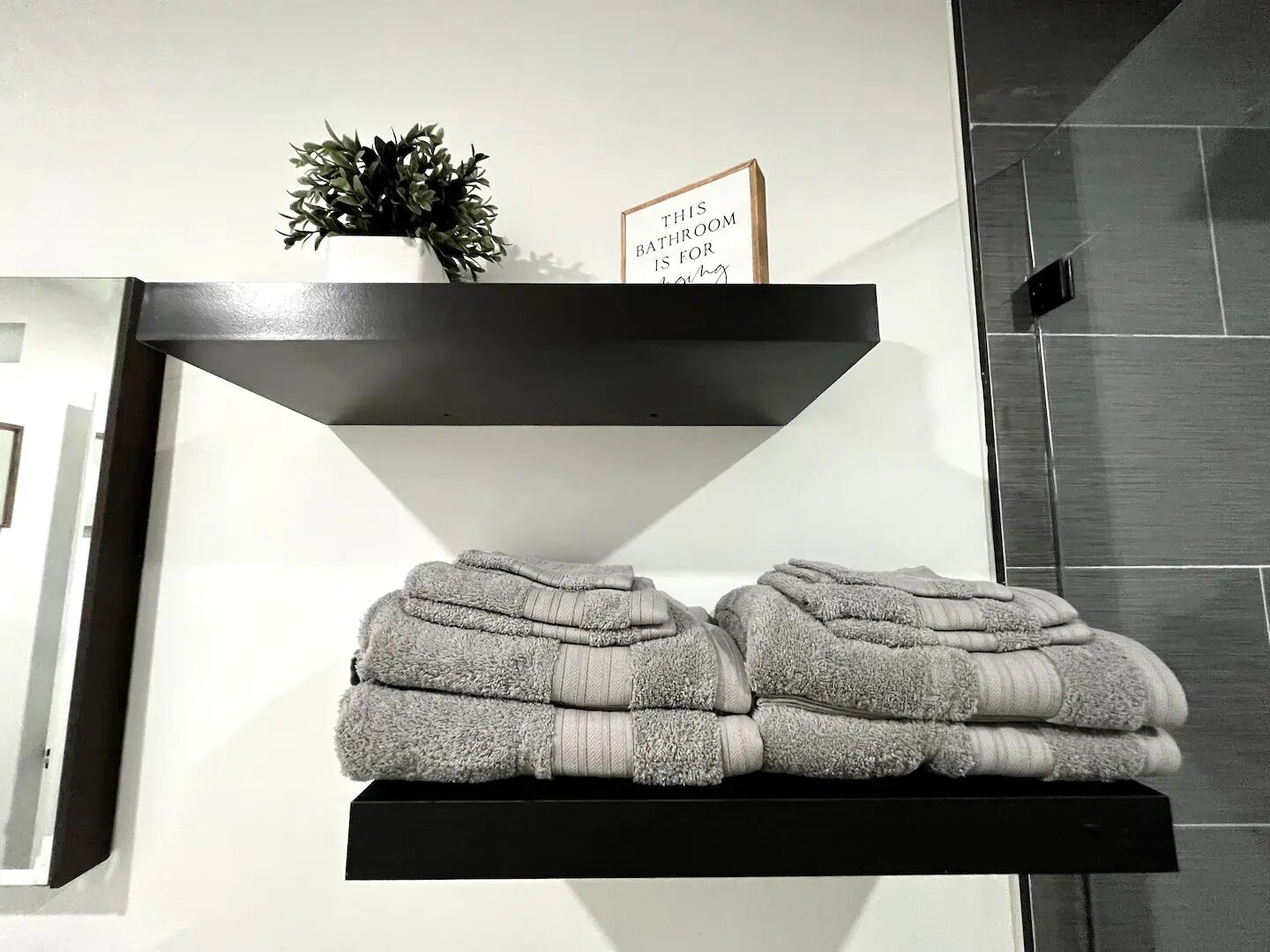 A black shelf with a potted plant and a sign, and folded towels below.
