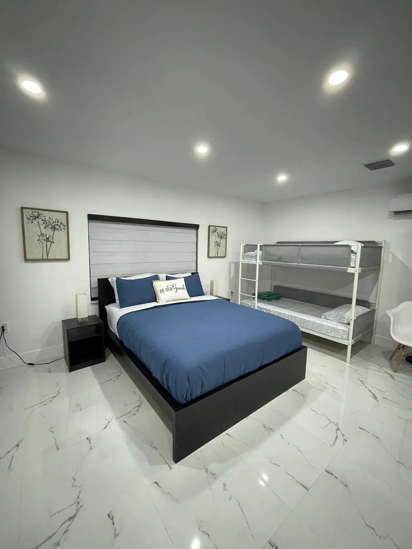 A modern bedroom with a large bed, a bunk bed, marble flooring, and wall-mounted artwork.