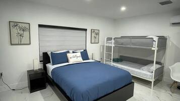 A modern bedroom with a large bed, a bunk bed, marble flooring, and wall-mounted artwork.