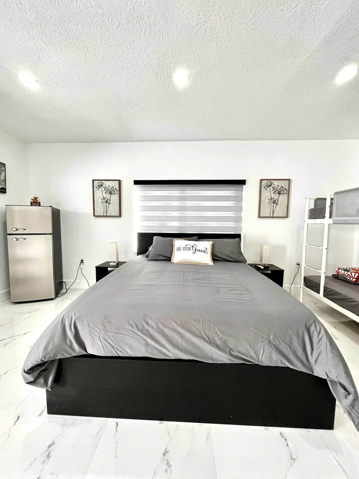 A modern bedroom with a large bed, bedside tables, a wardrobe, and a bunk bed.