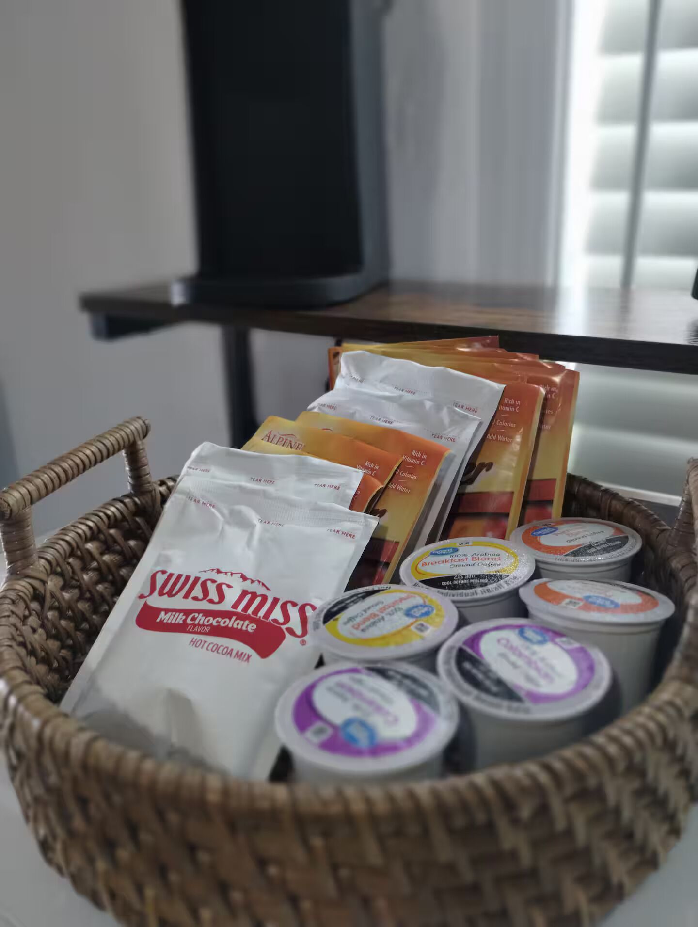 A wicker basket containing various food items including a Swiss Miss Milk Chocolate mix, Alpine brand snacks, and yogurt containers.