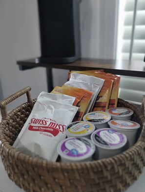 Un cesto di vimini contenente diversi prodotti alimentari, tra cui una miscela al cioccolato Alpine Swiss Miss, snack della marca Alpine e vasetti di yogurt.