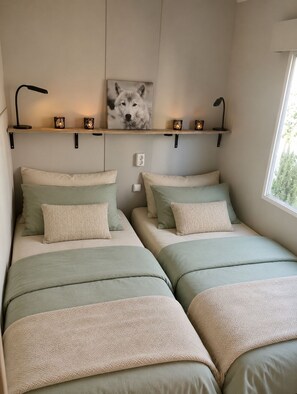 Een slaapkamer met twee bedden, een wandplank met decoratieve spullen, en een raam dat natuurlijk licht binnenlaat.