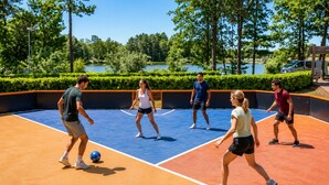 Una cancha de tenis con jugadores, rodeada de árboles y un cuerpo de agua.