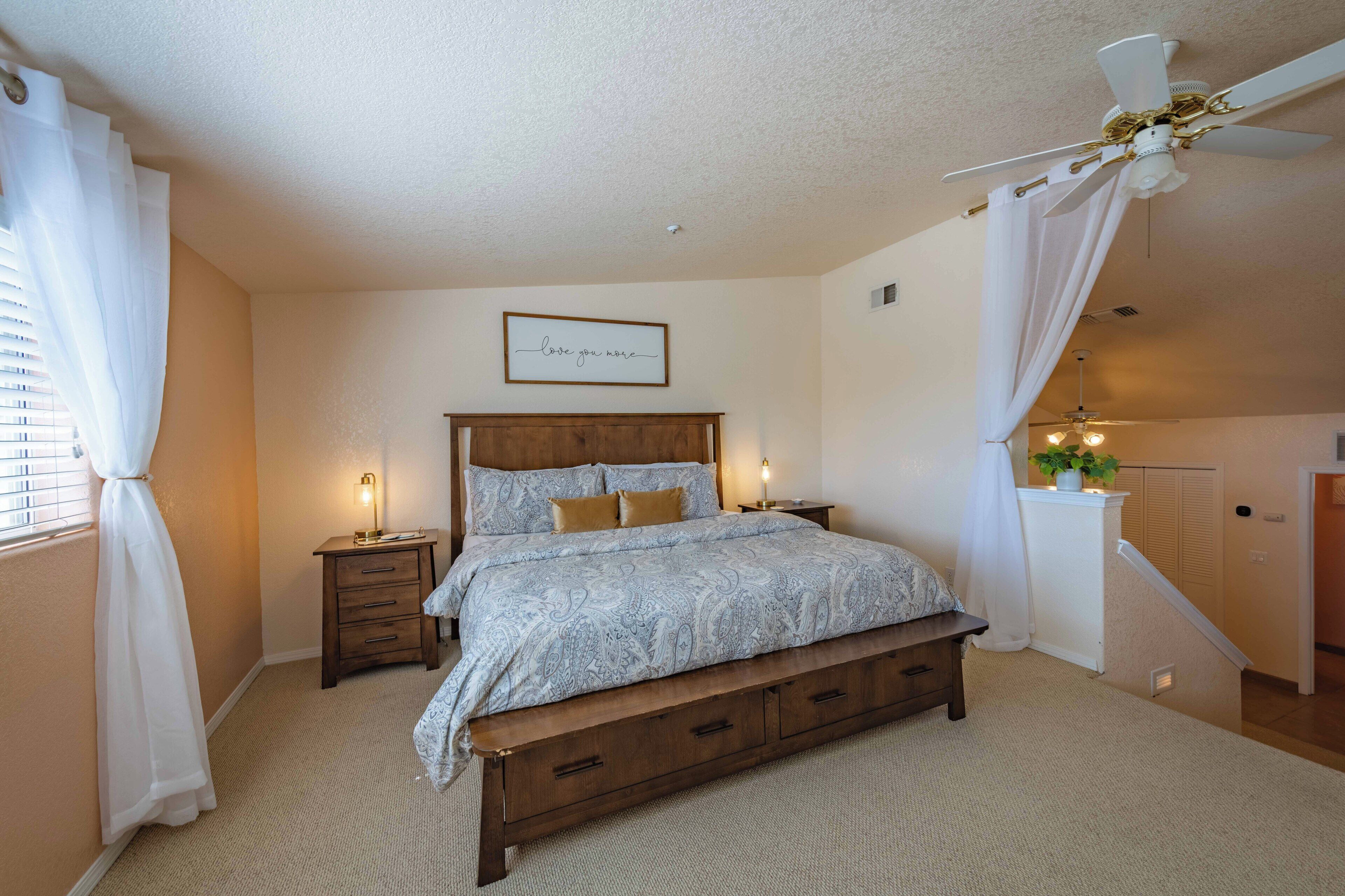 A bedroom with a bed, bedside tables, a ceiling fan, and a wall-mounted light fixture.