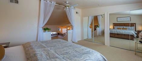 A bedroom with a large bed, a ceiling fan, a mirror, and a sliding glass door leading to another room.