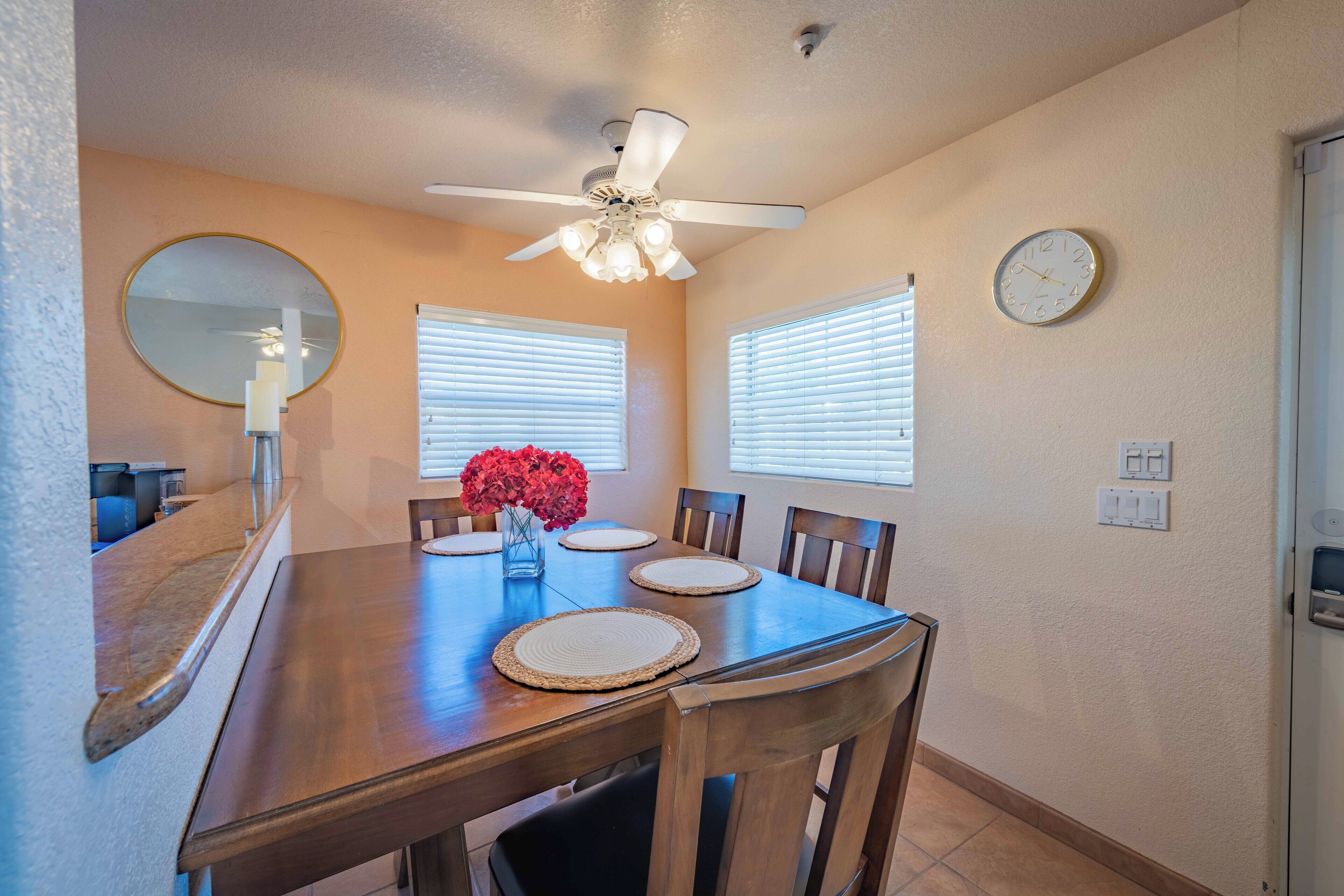A dining room with a wooden table, chairs, a ceiling fan, and a wall clock.