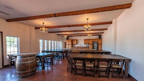 A spacious dining area with wooden tables and chairs, a large barrel, and a kitchen in the background. - Symphony Suite (Paso Robles)