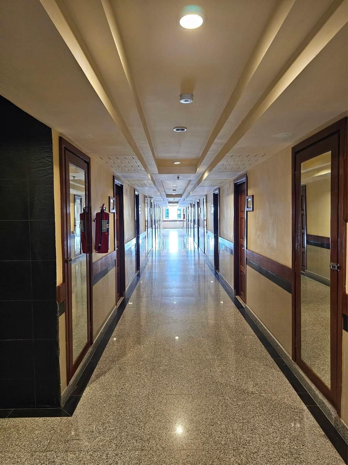 A long, well-lit hotel corridor with doors on both sides, leading to rooms.