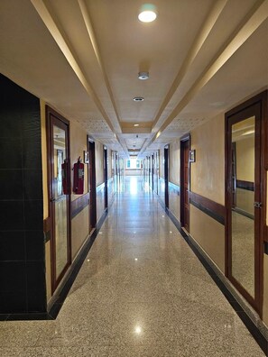 Un long couloir d’hôtel, bien éclairé, avec des portes des deux côtés, menant aux chambres.