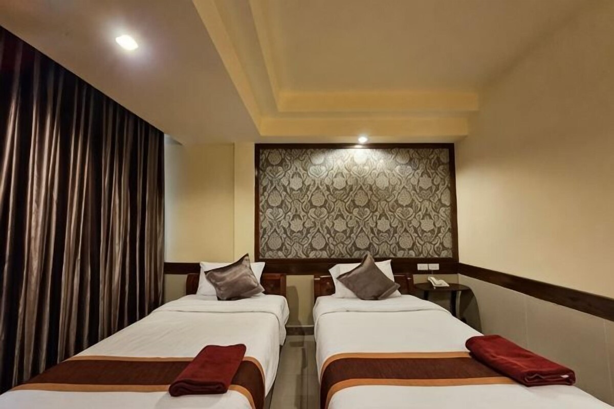 A hotel room with two beds, a patterned headboard, and a curtain on the left.