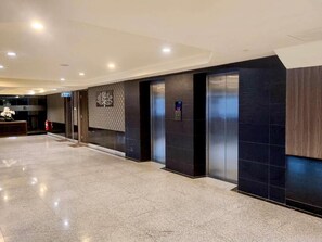 Un vestíbulo de hotel con una recepción, ascensores y una decoración de árbol montada en la pared.